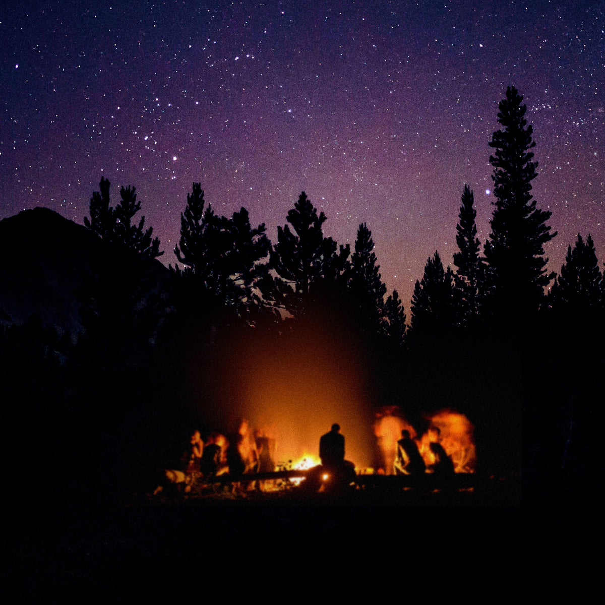 A star-filled night sky with a glowing campfire and silhouetted trees and people sitting beneath it, set against dark mountain hills.